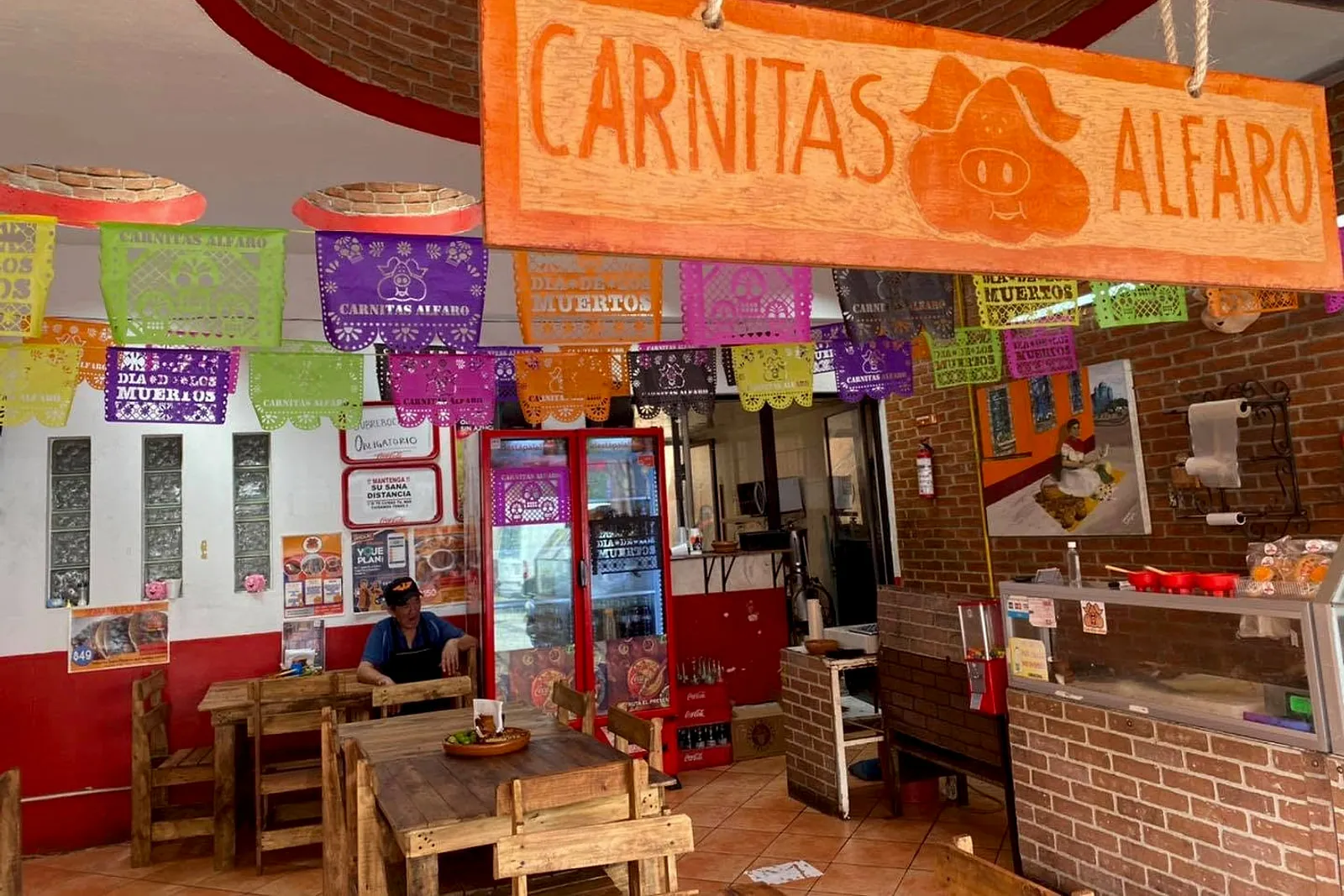 Interior de Carnitas Alfaro: pared de ladrillo, papel picado y letrero de madera